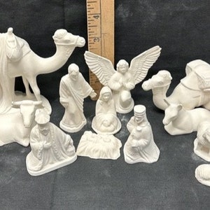 Puede incluir: Colección de figuras de cerámica sin pintar que representan un belén. El conjunto incluye figuras de camellos, ángeles, personas y animales. Las figuras son blancas y parecen listas para pintar.