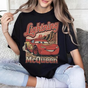 May include: Black t-shirt featuring a graphic of Lightning McQueen from the movie Cars. The design includes the text "Lightning McQueen" in a vintage style, with the number 95 on the car. The shirt is a crew neck.