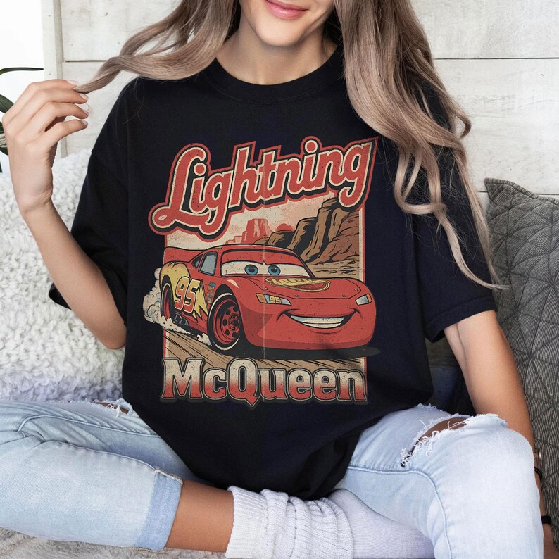May include: Black t-shirt featuring a graphic of Lightning McQueen from the movie Cars. The design includes the text "Lightning McQueen" in a vintage style, with the number 95 on the car. The shirt is a crew neck.
