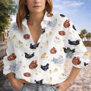 Puede incluir: Camisa blanca abotonada con un estampado repetido de gallinas de acuarela en varios colores. Las gallinas son marrones, negras, grises y amarillas. La camisa tiene mangas largas y cuello.