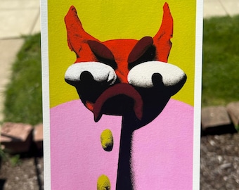 May include: A colorful art print featuring a stylized, cartoonish devil face with red horns, a dark frown, and large white eyes. The devil's face is set against a yellow background, with a pink shirt and two yellow oval shapes. The artwork has a bold, graphic style.