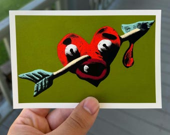 May include: A red heart pierced by an arrow, with a distressed, cartoonish design. The heart has white eyes and a wide open mouth, with a drop of red blood. The arrow has a blue-green arrowhead and a tan shaft, set against a green background.