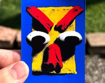 May include: A rectangular sticker featuring a vibrant blue border surrounding a yellow central block. The design displays a stylized face with two red angled eyebrows, two large white circular eyes with black pupils, and a red nose shape.