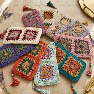 May include: A collection of colorful, handmade crochet pouches with zipper closures and tassel accents. The pouches feature a granny square design in various colors, including pink, orange, blue, and green. The pouches are arranged on a tiled surface.