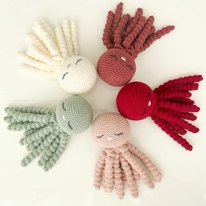 Könnte beinhalten: Fünf gehäkelte Octopus-Plüschtiere in verschiedenen Farben: Weiß, Rosa, Rot, Grün und Braun. Jeder Octopus hat ein lächelndes Gesicht mit geschlossenen Augen.