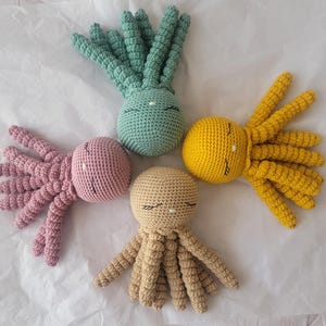Peut inclure: Quatre pieuvres crochetées de différentes couleurs : vert clair, rose, jaune et beige. Chaque pieuvre a une tête ronde avec des yeux fermés et plusieurs tentacules. Jouets faits à la main, adaptés aux enfants.