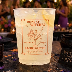 May include: A clear plastic cup filled with ice and a lemon slice, featuring orange text and a graphic of a person in a witch hat sitting in a martini glass. The text reads: Drink Up Witches, Welcome to Jenny's Bachelorette, August 1st, 2026.