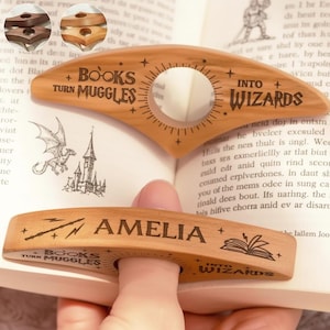 May include: Wooden book page holders with the text "BOOKS TURN MUGGLES INTO WIZARDS" and "AMELIA". The holders are light brown with a circular finger hole. One holder is in use, holding open a book.