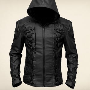 Puede incluir: Chaqueta de cuero negra con capucha y cremallera frontal. La chaqueta presenta detalles de cordones decorativos en la parte delantera y en las mangas. Los hombros tienen un diseño acolchado.