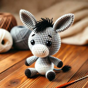 Puede incluir: Un juguete de burro de crochet gris y blanco con hilo negro para la crin y la cola. El juguete tiene grandes ojos negros y una nariz de crochet blanca.