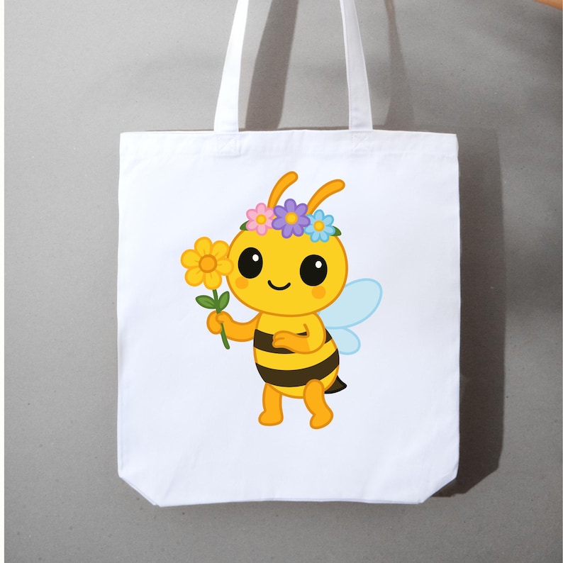 May include: White tote bag featuring a cartoon bee with a flower and a floral crown. The bee is yellow with black stripes, blue wings, and large black eyes. The tote bag has white handles and is made of a sturdy fabric.