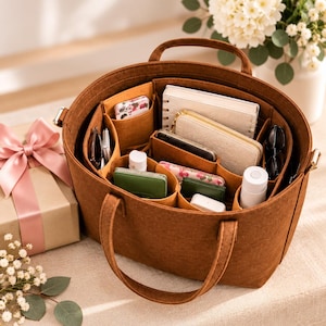 May include: A brown felt tote bag organizer with multiple interior compartments. The organizer is filled with various items including a white notebook, a beige wallet, a green case, a white bottle, and small personal accessories.
