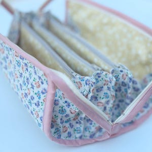 May include: A floral print organizer bag with a light pink trim and handles. The bag has multiple zippered compartments, each with a clear plastic front. The floral pattern includes blue, purple, and orange flowers on a white background.