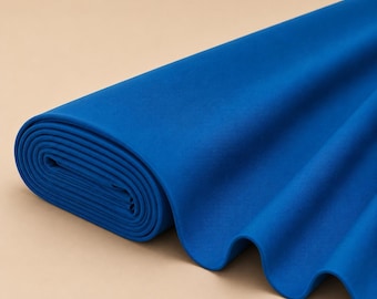May include: A bolt of solid royal blue fabric rolled tightly on one end with the remaining length draped in soft, smooth folds. The textile features a consistent, vibrant blue hue throughout, showcasing a matte finish and a clean, uniform texture.