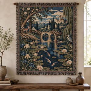 May include: A rectangular woven wall tapestry featuring a detailed landscape scene with a stone bridge, a castle in the distance, a deer, a heron, and koi fish swimming in a pond filled with water lilies, finished with a fringed border.