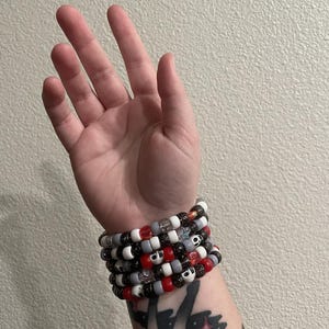 May include: A stack of colorful beaded bracelets with black, white, red, and gray beads. The bracelets feature skull-shaped beads and some beads have glitter.