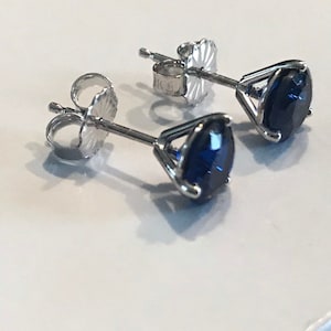 May include: A pair of silver stud earrings with dark blue gemstones. The gemstones are set in a prong setting.