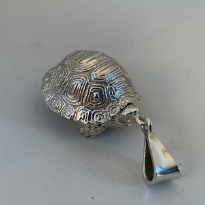 May include: A silver turtle pendant with a detailed shell design and a simple loop bail.