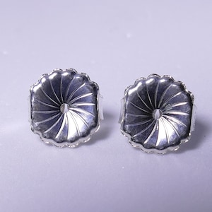 May include: Two silver-colored earring backs with a flower-like design. Each back has a scalloped edge and a central hole. The backs are designed to secure earrings and are displayed against a light background.