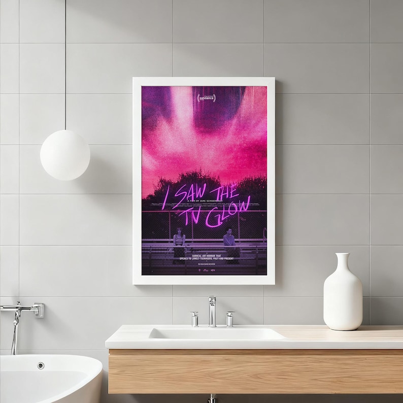 Op de afbeelding: Een ingelijste poster met de tekst "I SAW THE TV GLOW" in paars neon tegen een roze en zwarte achtergrond. De poster toont twee figuren en is geplaatst in een witte lijst.