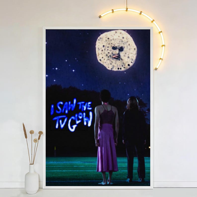 Op de afbeelding: Een ingelijste kunstdruk met een surrealistische nachtsc&egrave;ne. Twee figuren staan op een veld en kijken naar een maanachtig object in de lucht. De tekst "I SAW THE TV GLOW" is blauw verlicht. Het kunstwerk heeft een vintage, dromerige kwaliteit.
