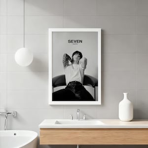 May include: Black and white framed print featuring a person seated in a chair, with the word "SEVEN" at the top. The person is wearing a white t-shirt and black pants. The image is displayed in a bathroom setting.