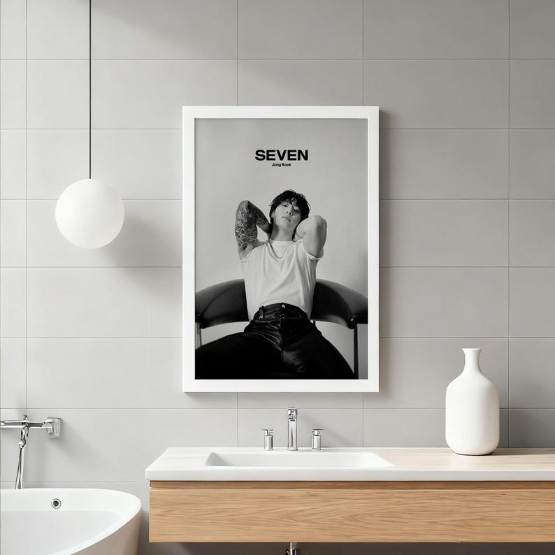 May include: Black and white framed print featuring a person seated in a chair, with the word "SEVEN" at the top. The person is wearing a white t-shirt and black pants. The image is displayed in a bathroom setting.
