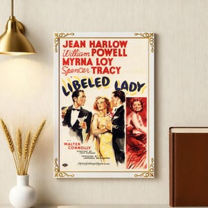 Pode incluir: Um cartaz de filme vintage emoldurado para "Libeled Lady" com Jean Harlow, William Powell, Myrna Loy e Spencer Tracy. O cartaz tem uma borda branca com detalhes dourados e inclui o título e os créditos do filme.