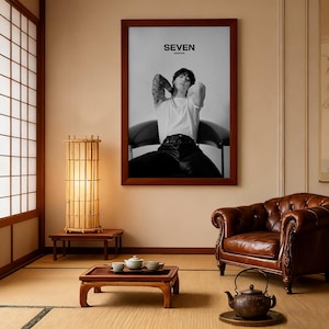 May include: A framed black and white poster with the word "SEVEN" at the top. The poster features a person in a white t-shirt and black pants. The room includes a bamboo lamp, a brown leather armchair, and a low wooden table.