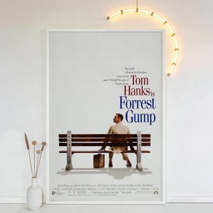 Op de afbeelding: Een ingelijste filmposter voor "Forrest Gump" met Tom Hanks. De poster toont een man die op een bankje zit met een koffer. De titel staat in grote, vette letters, met de quote "De wereld zal nooit meer hetzelfde zijn als je het door de ogen van Forrest Gump hebt gezien."