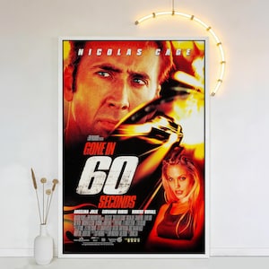 May include: A framed movie poster for "Gone in 60 Seconds" featuring Nicolas Cage and Angelina Jolie. The poster has a red and black background with the movie title in large, distressed white lettering. The actors' faces are prominently displayed.