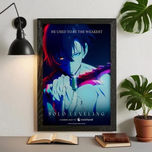 以下が含まれることがあります： 「ソロ・レベリング」のアニメアートが描かれた額入りポスター。青と赤の照明で照らされたキャラクターが武器を持っています。上部には「HE USED TO BE THE WEAKEST」、下部には「SOLO LEVELING」と「COMING 2023 TO crunchyroll」と書かれています。
