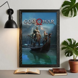 Może przedstawiać: Oprawiony wydruk artystyczny z gry wideo "God of War". Grafika przedstawia dwie postacie w łodzi na jeziorze, z tytułem gry u góry. Rama jest czarna, a wydruk jest wystawiony na biurku.