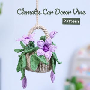 Könnte beinhalten: Gehäkelte Auto-Dekorationsranke mit einem Korb voller lila Clematisblüten und grünen Blättern, aufgehängt an einem beigen Seil. Der Text "Clematis Car Decor Vine Pattern" ist über dem Korb zu sehen.