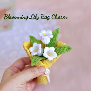 May include: A crocheted bag charm featuring a small bouquet of white calla lilies with yellow centres, green leaves, and a yellow wrapping. The text "Blooming Lily Bag Charm" is visible.