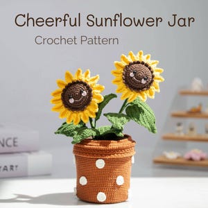 Puede incluir: Un tarro de girasol de crochet con dos girasoles sonrientes en una maceta marrón con lunares blancos. La maceta está sobre una superficie blanca.