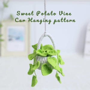 Può includere: Un modello di sospensione per auto all'uncinetto con una piccola pianta verde chiaro con foglie a forma di cuore in un vaso grigio. Il vaso è sospeso da un manico di corda bianca. Il testo "Sweet Potato Vine Car Hanging pattern" è sopra.