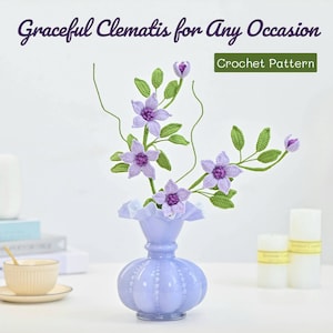 Könnte beinhalten: Eine gehäkelte Clematis-Blumenarrangements in einer hellblauen Vase. Die Blumen sind in einem blassen Lila mit grünen Blättern. Die Vase hat eine strukturierte Oberfläche und einen gekräuselten Rand. Der Text "Graceful Clematis for Any Occasion Crochet Pattern" befindet sich oben im Bild.