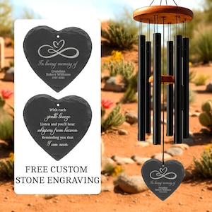 May include: A black wind chime with a wooden top and a heart-shaped slate stone. The stone is engraved with the text "In loving memory of Grandma Robert Williams 1957-2025". The image also shows two heart-shaped slate stones with engraved text.