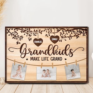May include: Wooden framed sign with the words "Grandkids Make Life Grand" in a decorative font. The sign includes three small photos clipped to a string, with the names "Charlie" and "Emily" above. The background has a wood grain pattern.
