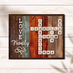 May include: Wooden framed wall art with the words "LOVE Family" and a heart symbol. The background is made of vertical wooden planks in various colors. Scrabble tiles spell out names including Isabella, Luna, Charlotte, and Emma.