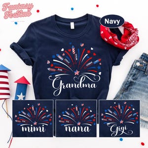 May include: Navy blue t-shirt with a firework design in red, white, and blue. The word "Grandma" is written in a script font. Additional shirts feature "Mimi", "Nana", and "Gigi" designs. A red bandana and denim shorts are also visible.
