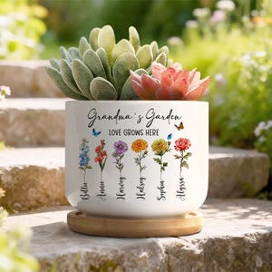 May include: A white ceramic plant pot with the text "Grandma's Garden" and "LOVE GROWS HERE." The pot features colourful flower illustrations and names. It holds a succulent plant and sits on a wooden base.