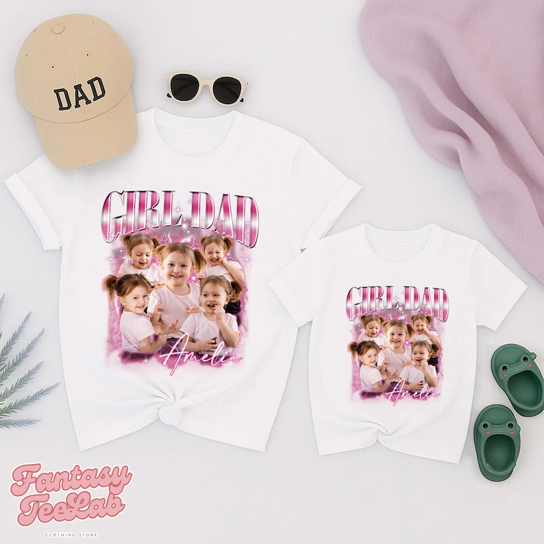 K&ouml;nnte beinhalten: Wei&szlig;e T-Shirts mit einem "GIRL DAD"-Aufdruck und einem Foto von jungen M&auml;dchen. Eine beige Baseballkappe mit "DAD" liegt obenauf. Sonnenbrillen und gr&uuml;ne Sandalen sind ebenfalls im Bild.