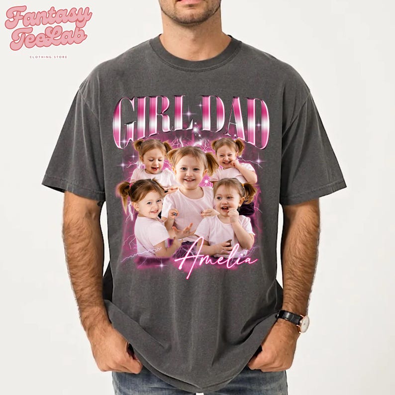 K&ouml;nnte beinhalten: Dunkelgraues T-Shirt mit einem rosa-wei&szlig;en Aufdruck "GIRL DAD" und einem Foto eines jungen M&auml;dchens namens Amelia. Das T-Shirt hat auch das Logo "Fantasy TeeLab" oben links.