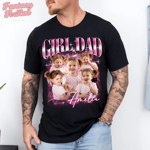 K&ouml;nnte beinhalten: Schwarzes T-Shirt mit einem rosa-wei&szlig;en "GIRL DAD"-Aufdruck und einer Fotocollage von f&uuml;nf l&auml;chelnden jungen M&auml;dchen. Der Name "Amelia" ist darunter in rosa Schrift geschrieben. Das T-Shirt stammt vom Fantasy TeeLab Bekleidungsgesch&auml;ft.