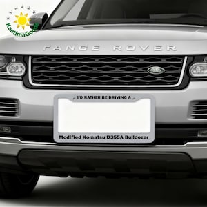 Puede incluir: Un Range Rover plateado con una parrilla negra y un marco de matr&iacute;cula que dice "I'D RATHER BE DRIVING A" y "Modified Komatsu D355A Bulldozer."