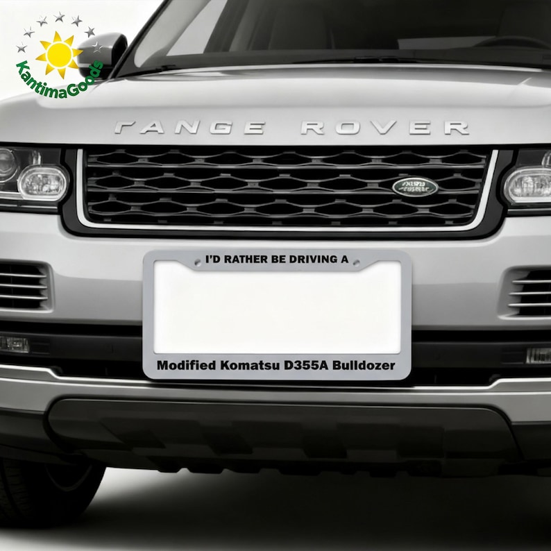 Puede incluir: Un Range Rover plateado con una parrilla negra y un marco de matr&iacute;cula que dice "I'D RATHER BE DRIVING A" y "Modified Komatsu D355A Bulldozer."