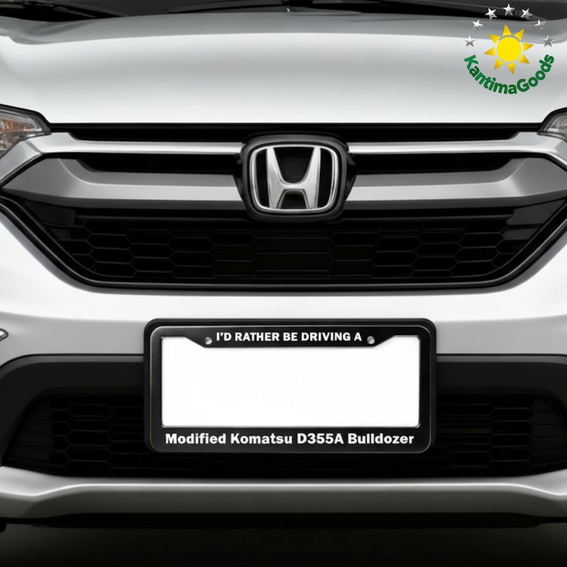 Puede incluir: Primer plano de la parte delantera de un coche, con un marco de matr&iacute;cula negro con el texto "I'D RATHER BE DRIVING A" y "Modified Komatsu D355A Bulldozer". El coche tiene una parrilla negra y un emblema de Honda.