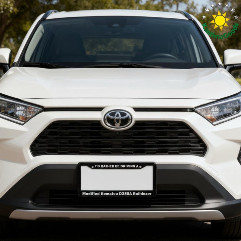 Puede incluir: Un SUV Toyota blanco con una parrilla negra y una placa que dice "I'D RATHER BE DRIVING A" y "Modified Komatsu D355A Bulldozer". El logotipo de Toyota es visible en la parte delantera.